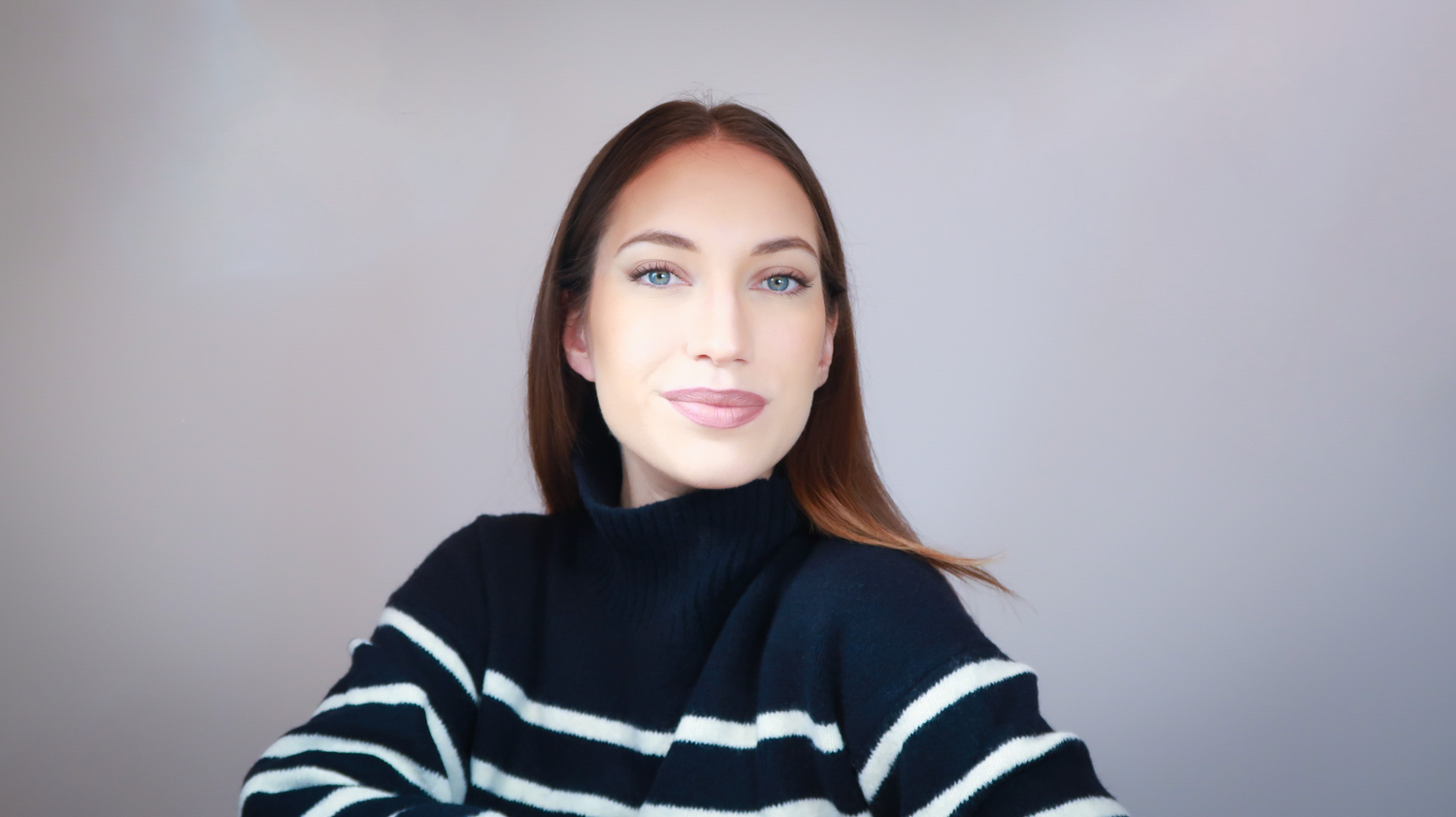 Portrait de Coline, créatrice de press on nails, posant avec un léger sourire sur un fond gris clair dans une ambiance studio, incarnant l’élégance et le savoir-faire des faux ongles faits main.